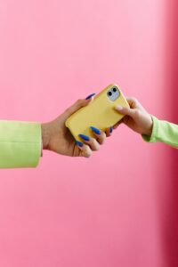 paznokcie baby blue dwie dłonie trzymające telefon w żółtym etui na różowym tle